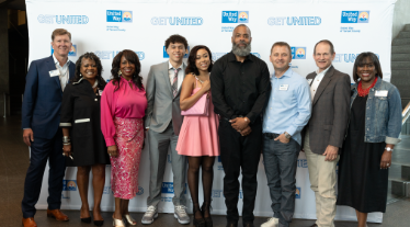 Representatives from Interbank and United Way of Tarrant County smile for a photo alongside The DOC and his daughter Puma.