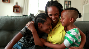 Mother hugging two children on sofa.