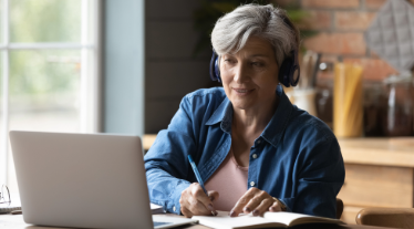 Older adult watching computer class, taking notes. 