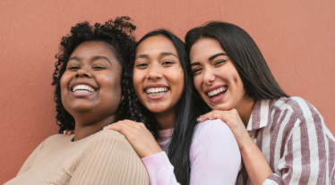 Group of three women smiling in front of wall.