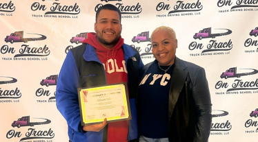 Rolando Nieto with Kenya Mobley holding his CDL certificate in front of a backdrop with logos for On Track Trucking School